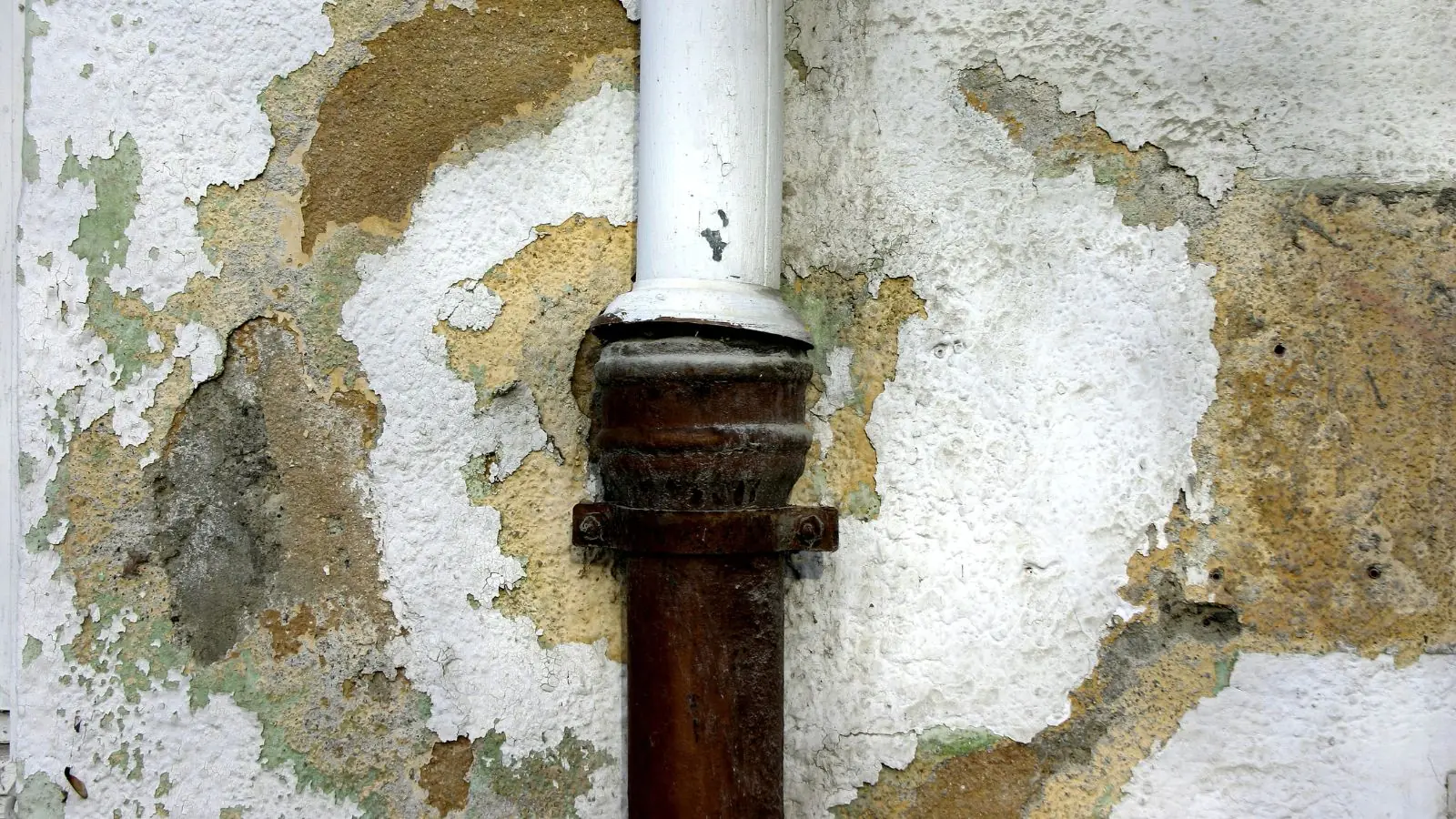 Rusted drain pipe with peeling paint and crumbling plaster around it