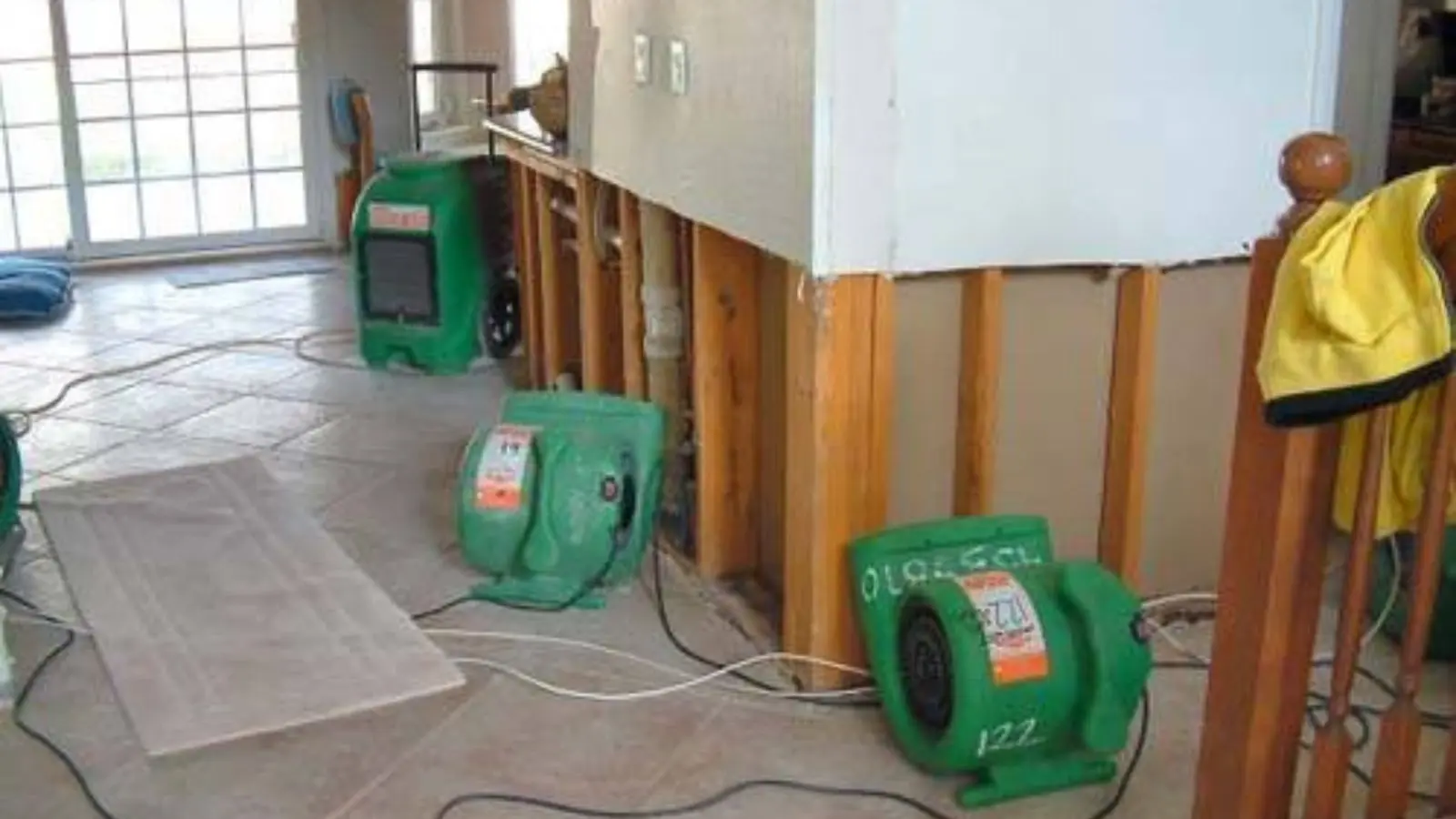 Air movers running in a room where the lower wall has been cut open to dry the cavity