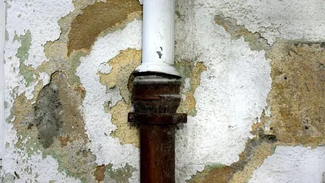 Rusted drain pipe with peeling paint and crumbling plaster around it