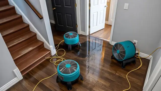 Three air movers drying a wet hardwood floor beside a staircase